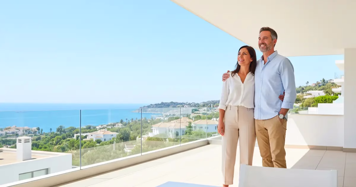 Couple visitant un appartement moderne en Espagne avec vue sur la mer Méditerranée, illustrant le financement immobilier en 2025