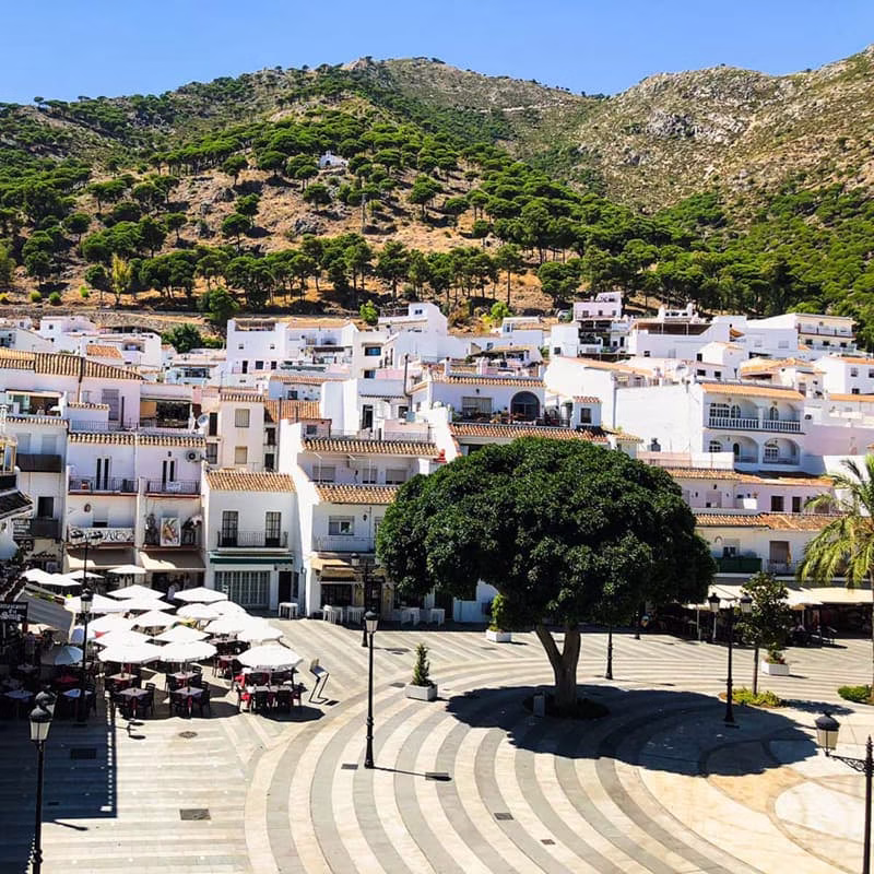 Place centrale de Mijas Place centrale de Mijas avec terrasses ombragées, maisons blanches et collines verdoyantes à l’horizon