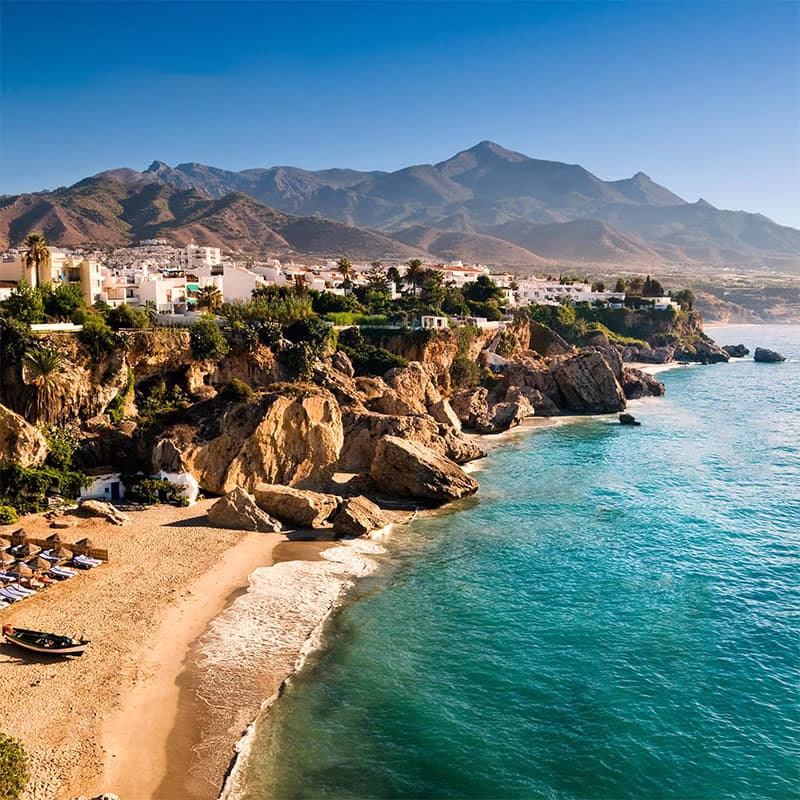 Plage de Nerja Plage pittoresque de Nerja bordée de falaises, avec des montagnes en arrière-plan et des eaux cristallines