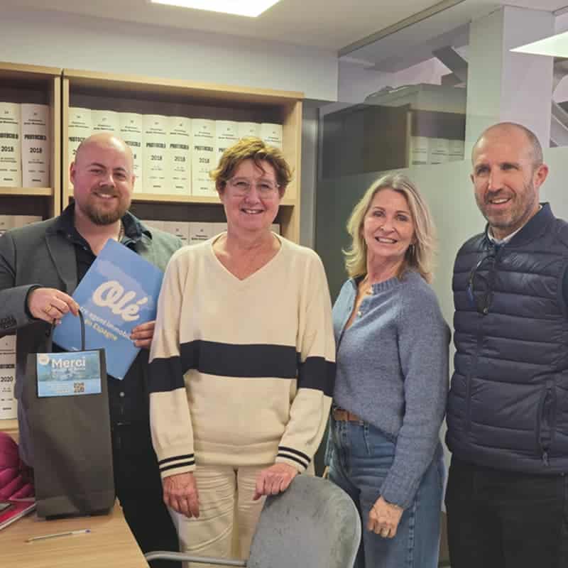 Quatre personnes souriantes posant dans un bureau, un homme tient un dossier Olé