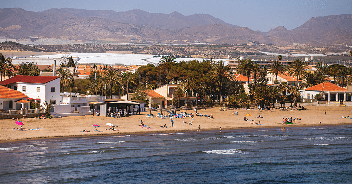 Plage de Mazarrón sur la Costa Cálida, avec maisons en bord de mer, palmiers, baigneurs et montagnes en arrière-plan