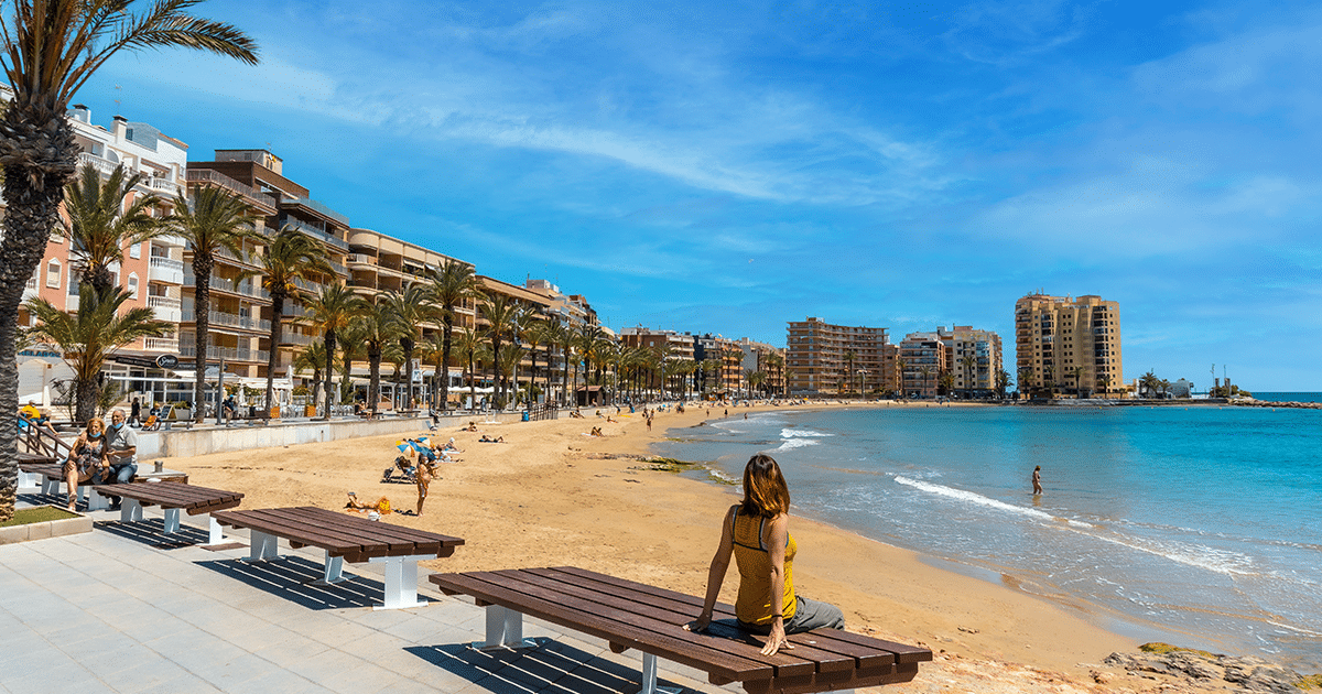 Vue de la plage de Torrevieja avec promenade bordée de palmiers, immeubles résidentiels et baigneurs sous le soleil de la Costa Blanca