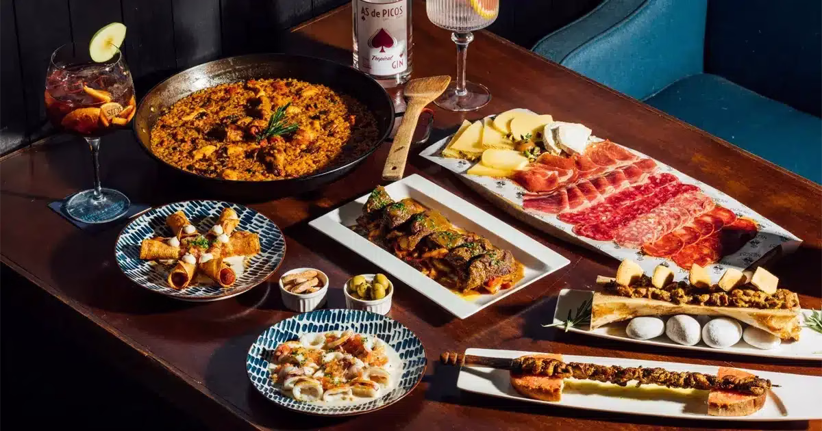 Table garnie de spécialités espagnoles avec paella, tapas, charcuterie et fromage, accompagnés de cocktails