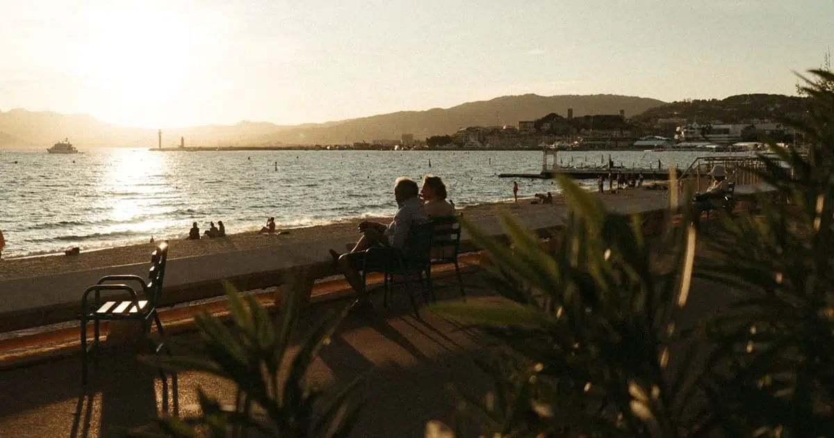 Couple de retraités assis face à la mer au coucher du soleil, illustrant des modes de vie variés et un rythme de vie adaptable en Espagne.